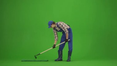 Bahçıvanlık ve tarım reklamları konsepti. Tulumlu erkek portresi ve krom anahtar yeşil ekranda lastik çizmeler. Erkek bahçıvan bir çapayla zemini gevşetiyor, terini silmekten yorgun görünüyor..
