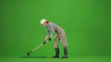 Bahçıvanlık ve tarım reklamları konsepti. Krom anahtar yeşil ekranda önlüklü kadın portresi ve lastik çizmeler. Kadın bahçıvan zemini çapayla düzleştiriyor, olumlu bir ifadeyle bakıyor..