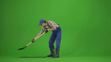 Bahçıvanlık ve tarım reklamları konsepti. Tulumlu erkek portresi ve krom anahtar yeşil ekranda lastik çizmeler. Bahçıvan adam kürekle toprağı kazıyor, bakıyor..