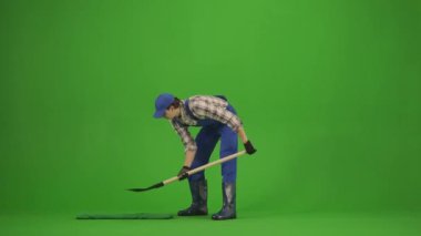 Bahçıvanlık ve tarım reklamları konsepti. Tulumlu erkek portresi ve krom anahtar yeşil ekranda lastik çizmeler. Bahçıvan adam yere kürekle çukur kazıyor, toprağı fırlatıyor..