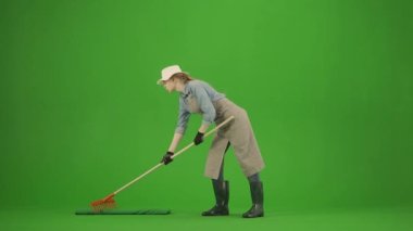Bahçıvanlık ve tarım reklamları konsepti. Krom anahtar yeşil ekranda önlüklü kadın portresi ve lastik çizmeler. Kadın bahçıvan zemini tırmıkla düzleştiriyor, yorgun bir ifadeyle bakıyor..