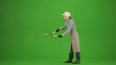 Bahçıvanlık ve tarım reklamları konsepti. Krom anahtar yeşil ekranda önlüklü kadın portresi ve lastik çizmeler. Bahçıvan kadın bahçe makasıyla çalıları buduyor, sonuçlara bakıyor..