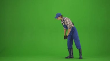 Bahçıvanlık ve tarım reklamları konsepti. Tulumlu erkek portresi ve krom anahtar yeşil ekranda lastik çizmeler. Erkek bahçıvan bitkilerine bakıyor, olumlu bir ifade..