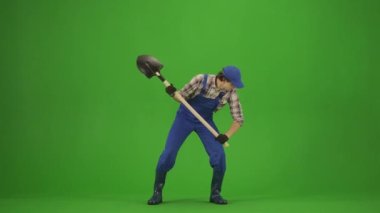 Bahçıvanlık ve tarım reklamları konsepti. Tulumlu erkek portresi ve krom anahtar yeşil ekranda lastik çizmeler. Ellerinde kürekle bahçıvan bir köstebek avlar, kenarlara bakar yorgun..