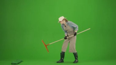 Bahçıvanlık ve tarım reklamları konsepti. Krom anahtar yeşil ekranda önlüklü kadın portresi ve lastik çizmeler. Kadın bahçıvan elinde tırmıkla bir köstebeği avlar, korkmuş yüzüne bakar..