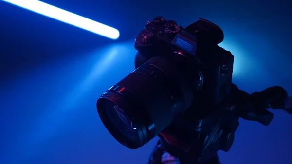 Professional photo camera stands on a tripod in a studio with color neon lighting