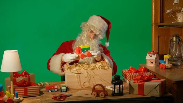 Święty Mikołaj Przy Stole Trzyma Drewnianą Zabawkę Dłoniach Zielonym Tle — Zdjęcie stockowe