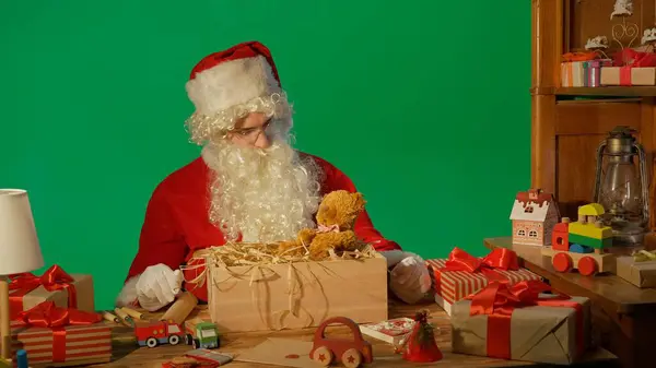Noel Baba Hediyelerle Masada Yeşil Arka Plandaki Oyuncak Ayıya Bakıyor — Stok fotoğraf