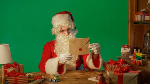 Noel Baba Hediyelerle Masada Yeşil Bir Arkaplanda Bir Mektup Okuyor — Stok fotoğraf