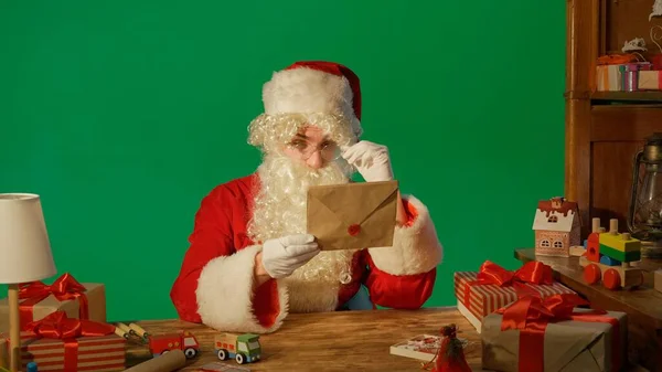 Święty Mikołaj Przy Stole Prezentami Czytając List Zielonym Tle — Zdjęcie stockowe