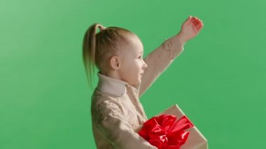 Stüdyodaki sarı arka plan duvarına izole edilmiş bir şekilde poz veren küçük şirin bir kız çocuğu. Şaşırmak için elini sallıyor. Noel konsepti.