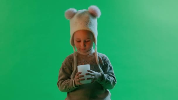 帽子をかぶった少女は 緑色の背景にあるろうそくを見ている クリスマスコンセプト — ストック動画