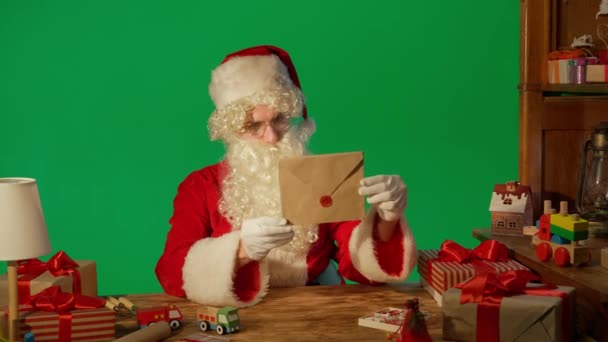 圣诞老人带着礼物坐在桌旁 带着绿色背景的信阅读着 — 图库视频影像