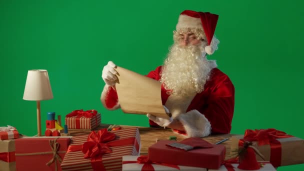 圣诞老人带着礼物坐在桌旁 阅读着绿色背景的信件 — 图库视频影像
