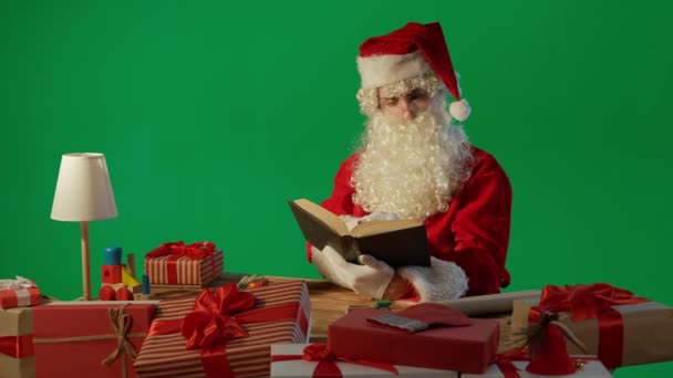 Święty Mikołaj Przy Stole Prezentami Czytając Książkę Bajkami Zielonym Tle — Wideo stockowe