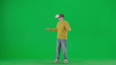 Modern çocuk okulu ve eğlence zamanı reklam konsepti. Krom anahtar yeşil ekrandaki çocuk portresi. Sanal gerçeklik gözlüklü, sıradan giysiler içinde duran ve şaşkın bakışlı okul çocuğu..
