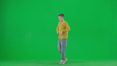 Modern çocuk okulu ve eğlence zamanı reklam konsepti. Krom anahtar yeşil ekrandaki çocuk portresi. Gündelik kıyafetlerle dans eden okul çocuğu modern moda dansı, havalı bir ifade, gülen surat..
