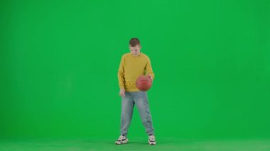Modern çocuk okulu ve eğlence zamanı reklam konsepti. Krom anahtar yeşil ekrandaki çocuk portresi. Normal giyimli okul çocuğu basketbol topuyla oynuyor, parmağında sallıyor..