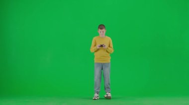 Modern çocuk okulu ve eğlence zamanı reklam konsepti. Krom anahtar yeşil ekrandaki çocuk portresi. Gündelik giysiler içinde okul çocuğu joystick ile video oyunu oynuyor, onu mutlu yüz ve jest ile kazanıyor..
