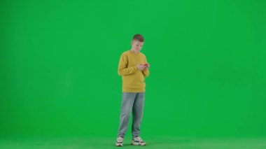 Modern çocuk okulu ve eğlence zamanı reklam konsepti. Krom anahtar yeşil ekrandaki çocuk portresi. Okul çocuğu günlük giysiler içinde elinde akıllı bir telefonla internetten komik videolar izliyor ve gülümsüyor..