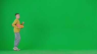 Modern çocuk okulu ve eğlence zamanı reklam konsepti. Krom anahtar yeşil ekrandaki çocuk portresi. Gündelik giysiler içinde elinde kaykayla yürüyen, el sallayan arkadaşlarıyla selamlaşan bir okul çocuğu..
