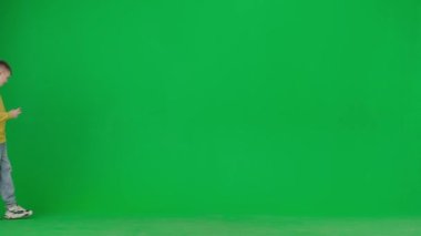 Modern çocuk okulu ve eğlence zamanı reklam konsepti. Krom anahtar yeşil ekrandaki çocuk portresi. Günlük kıyafetlerle gezen ve akıllı telefondan video oyunu oynayan okul çocuğu..