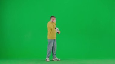 Modern çocuk okulu ve eğlence zamanı reklam konsepti. Krom anahtar yeşil ekrandaki çocuk portresi. Okul çocuğu günlük kıyafetlerle futbol topu tutuyor ve ailesiyle akıllı telefondan konuşuyor..