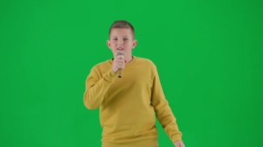 Modern çocuk okulu ve eğlence zamanı reklam konsepti. Krom anahtar yeşil ekrandaki çocuk portresi. Karaoke mikrofonunda şarkı söyleyip dans eden, mutlu ve ifadesiz bir öğrenci. Orta çekim.