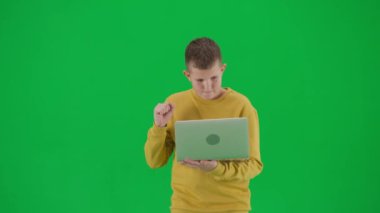 Modern çocuk okulu ve eğlence zamanı reklam konsepti. Krom anahtar yeşil ekrandaki çocuk portresi. Dizüstü bilgisayar tutan öğrenci, sonuçları bekliyor, mutlu yüz ifadesi kazanan bir jest. Orta çekim.