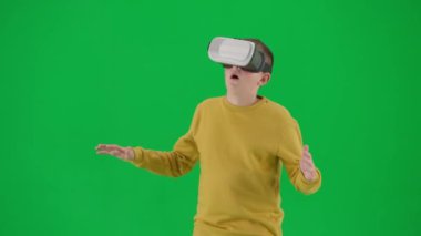 Modern çocuk okulu ve eğlence zamanı reklam konsepti. Krom anahtar yeşil ekrandaki çocuk portresi. Sanal gerçeklik gözlükleriyle ayakta duran ve şaşkın bakışlı öğrenci. Orta çekim.