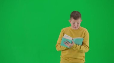 Modern çocuk okulu ve eğlence zamanı reklam konsepti. Krom anahtar yeşil ekrandaki çocuk portresi. Gündelik giyinmiş öğrenci. Şaşırmış bir yüz ifadesi olan bir kitap okuyor. Orta çekim.