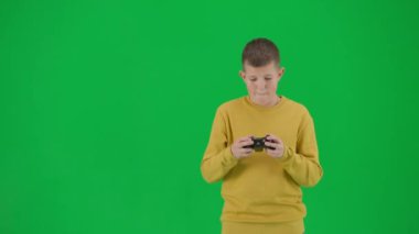 Modern çocuk okulu ve eğlence zamanı reklam konsepti. Krom anahtar yeşil ekrandaki çocuk portresi. Sıradan giyinen okul çocuğu joystick 'le video oyunu oynuyor, mutlu bir yüz ve jest kazanıyor. Orta çekim.