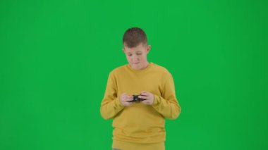Modern çocuk okulu ve eğlence zamanı reklam konsepti. Krom anahtar yeşil ekrandaki çocuk portresi. Sıradan giyinen okul çocuğu joystick ile video oyunu oynuyor, üzgün yüzünü ve jestini kaybediyor. Orta çekim.