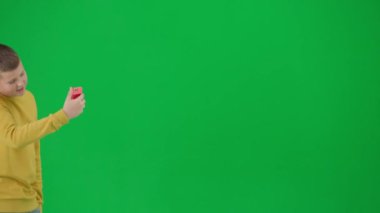 Modern çocuk okulu ve eğlence zamanı reklam konsepti. Krom anahtar yeşil ekrandaki çocuk portresi. Gündelik yürüyüşler yapan ve aileleriyle telefon görüşmesinde görüntülü konuşan öğrenci. Orta çekim.