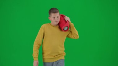 Modern çocuk okulu ve eğlence zamanı reklam konsepti. Krom anahtar yeşil ekrandaki çocuk portresi. Sıradan yürüyüşler yapan, elinde kırmızı müzik hoparlörü olan ve müzik dinleyen bir öğrenci. Ön çekim..