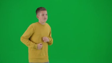 Modern çocuk okulu ve eğlence zamanı reklam konsepti. Krom anahtar yeşil ekrandaki çocuk portresi. Gündelik giysiler içinde koşuşturan ve etrafa bakınan okul çocuğu, ciddi bir yüz ifadesi. Profil fotoğrafı.