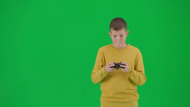 現代の子供の学校とレジャー時間の広告の概念 クロマキーグリーンスクリーンの少年肖像画 カジュアルなボーイはジョイスティックでビデオゲームをプレイし 幸せな顔とジェスチャーを獲得します ミドルショット — ストック動画
