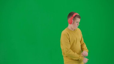 Okul çocukları ve eğlence zamanı yaratıcı konsepti. Krom anahtar yeşil ekranda çocuk portresi. Kot pantolonlu, kulaklıklı, dans eden, müzik dinleyen bir öğrenci. Orta gövde vuruşu.