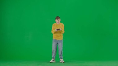 Okul çocukları ve eğlence zamanı yaratıcı konsepti. Krom anahtar yeşil ekranda çocuk portresi. Kotlu okul çocuğu elinde joystickle video oyunu oynuyor ve kameraya bakıyor. Tam vücut ön çekim.