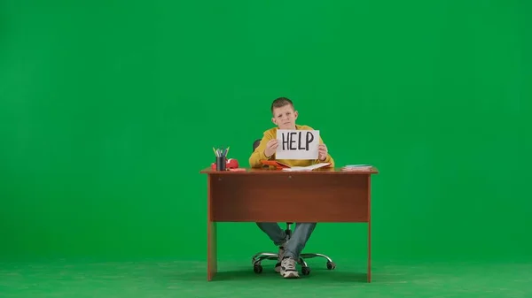 学校の子供たちと余暇の時間創造的なコンセプト クロマキーグリーンスクリーンの子供の肖像画 机に座っているジーンズの少年が宿題をし 手紙のサインを握る フルフロントショット — ストック写真