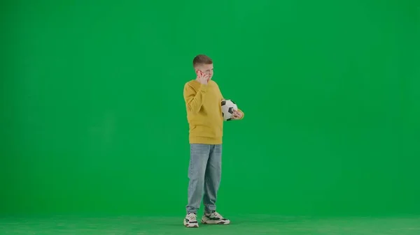 学生和闲暇时间的创意概念 彩色键绿色屏幕上的小男孩的肖像 穿着牛仔裤的男孩拿着足球 用智能手机说话 全身而退 — 图库照片