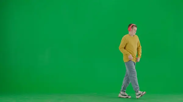 学生和闲暇时间的创意概念 彩色键绿色屏幕上的小男孩的肖像 穿着牛仔裤 头戴耳机的男孩一边走路一边跳舞 听着音乐 全身而退 — 图库照片