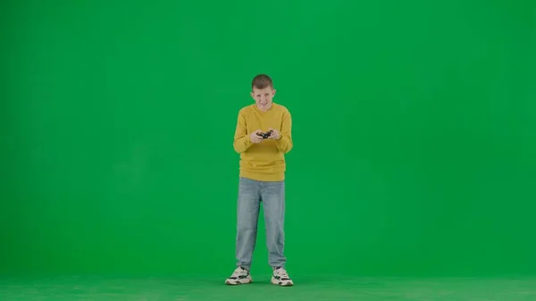 学生和闲暇时间的创意概念 彩色键绿色屏幕上的小男孩的肖像 穿着牛仔裤的男孩拿着操纵杆 玩电子游戏 看着镜头 全身上下正中枪 — 图库照片