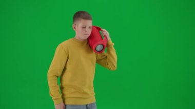 Modern çocuk okulu ve eğlence zamanı reklam konsepti. Krom anahtar yeşil ekrandaki çocuk portresi. Sıradan yürüyüşler yapan, elinde kırmızı müzik hoparlörü olan ve müzik dinleyen bir öğrenci. Profil fotoğrafı.