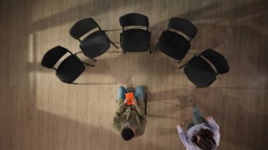 Yukarıdaki çerçevede, orta yaşlı bir adam elinde bir defterle ortada oturuyor. Sonra insanlar karşılarına oturur, terapi için bir psikologla görüşmeye gelirler. Sorunları tartışıyorlar..