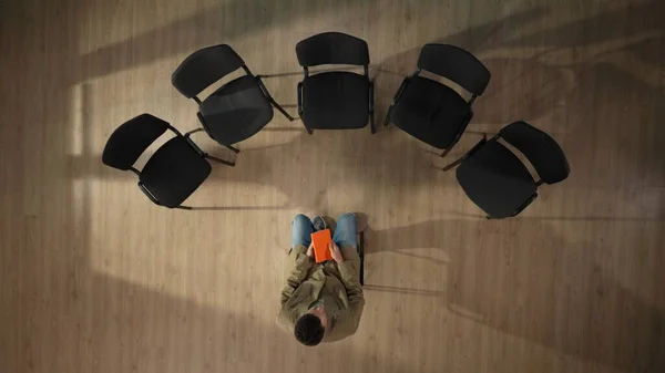 上のフレームでは 中年男性が中央に椅子に座っています 彼のグループミーティングが始まり 何かを考え 考え始めるのを待っている 彼はオレンジのノートを持っている トップビュー — ストック写真