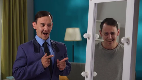 分裂した性格に苦しむ緊張したスーツを着た男は 鏡の前にあるリビングに立っている 二番目の性格が彼を嘲笑する スプリットパーソナリティ — ストック写真