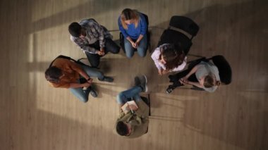 Yukarıdaki çekimde, bir grup terapi seansında oturuyor. Karşılarında bir psikiyatrist oturuyor, sohbet ediyor ve onları dinliyor. Genç bir kadın ayağa kalkıyor ve bir sorunu paylaşıyor. Destekleniyor..