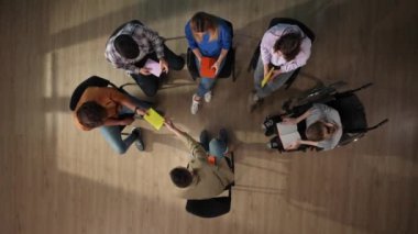 Yukarıdaki çekimde, bir grup insan ve akıl hocaları bir sandalyede oturuyorlar. Terapi için geldiler. Bir çemberde oturup engelli biriyle deftere bir şeyler yazıyorlar..