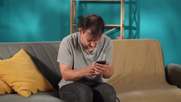 Nerwowy Mężczyzna Siedzi Kanapie Salonie Używając Smartfona Grając Grę Online — Wideo stockowe